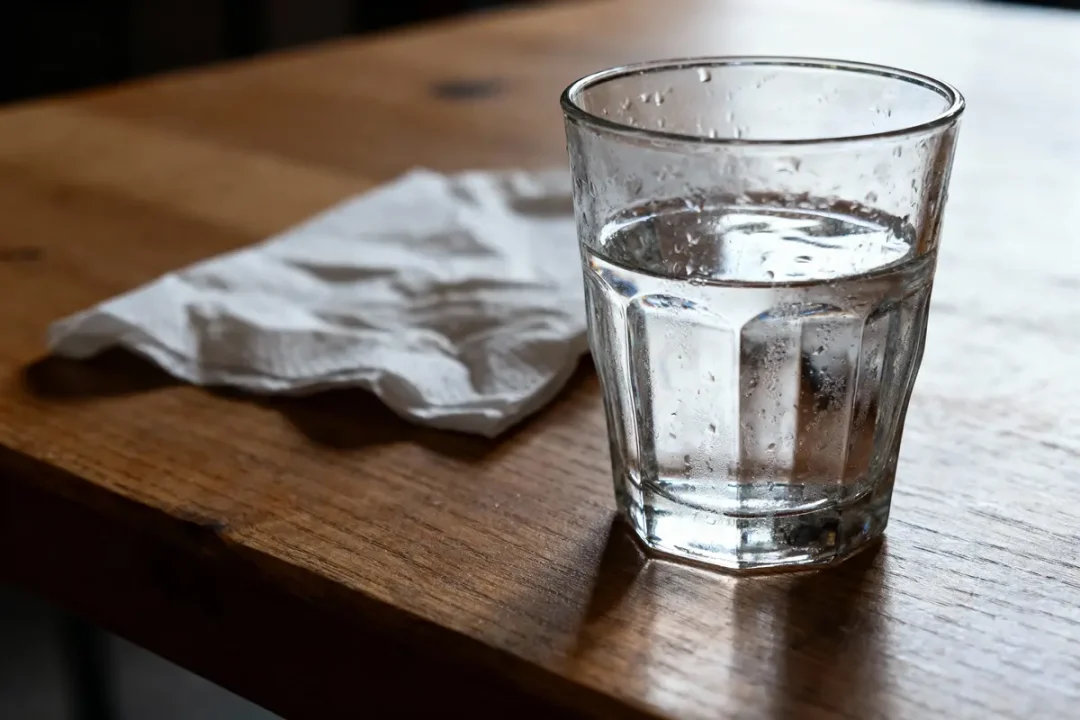 Verre d'eau et serviette en papier sur table en bois.