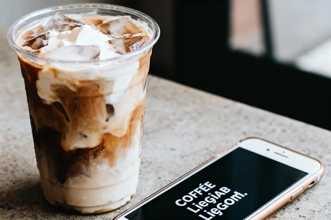Boisson glacée au café avec crème, posée à côté d'un smartphone sur une table.