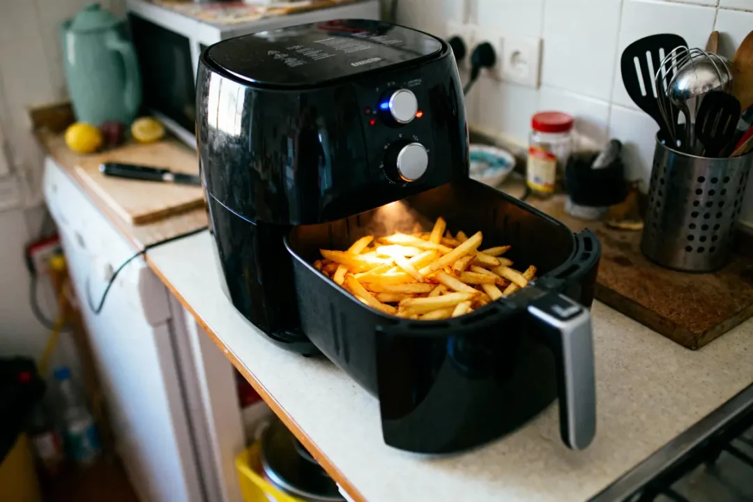 Friteuse à air noir, préparant des frites dorées dans une cuisine avec ustensiles et planche à découper.