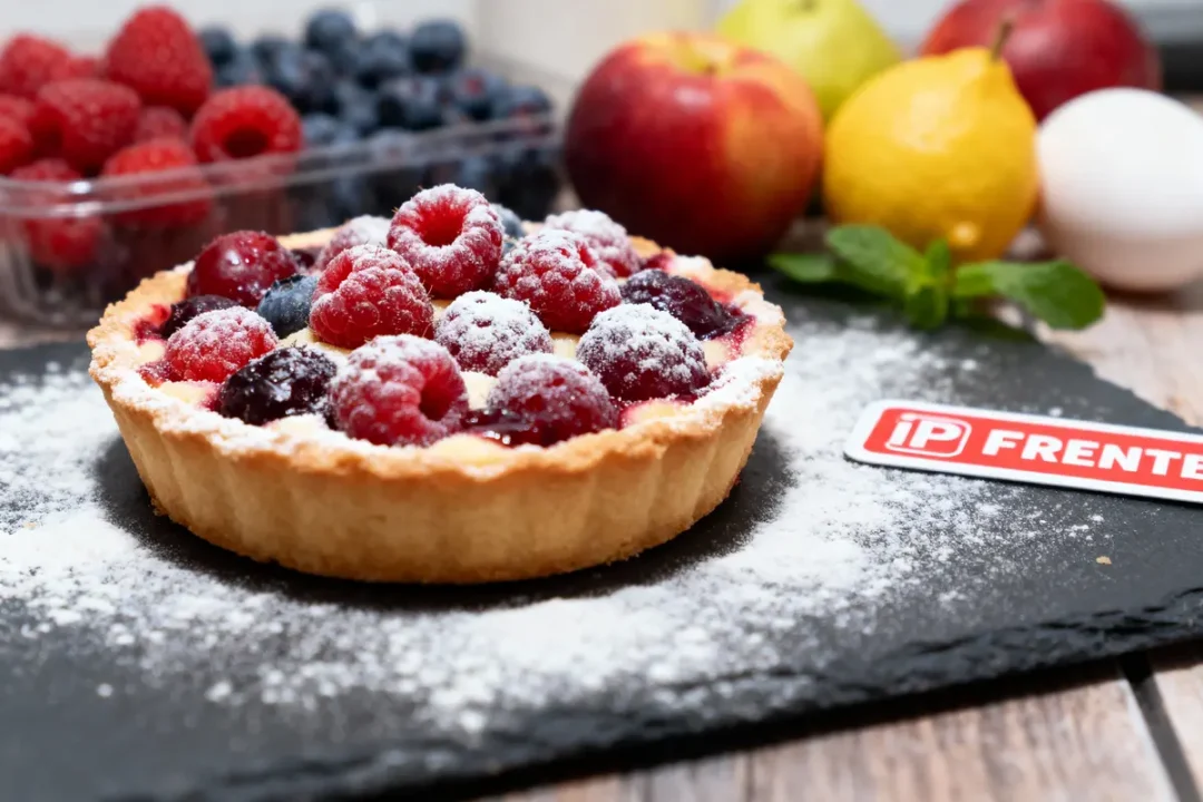 Tarte aux fruits rouges sur ardoise, poudrée de sucre glace, entourée de fruits frais et menthe.