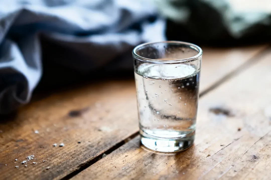 Verre d'eau pétillante sur table en bois, tissu flou en arrière-plan.