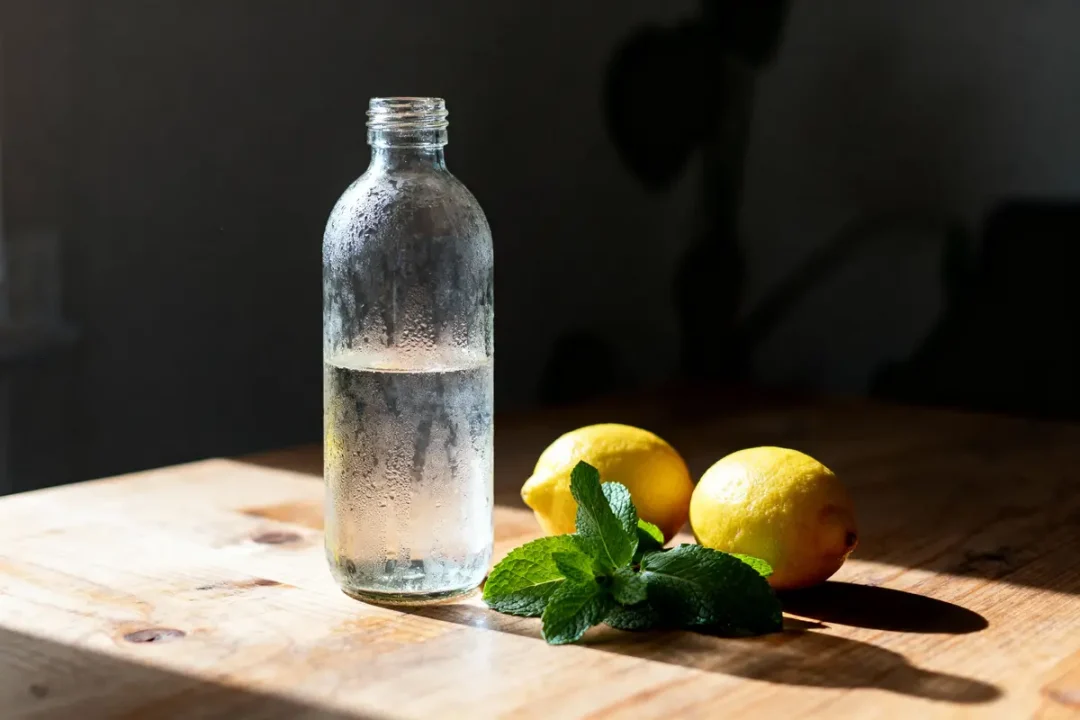 Bouteille d'eau avec condensation, citrons jaunes et feuille de menthe sur table en bois, éclairage naturel.