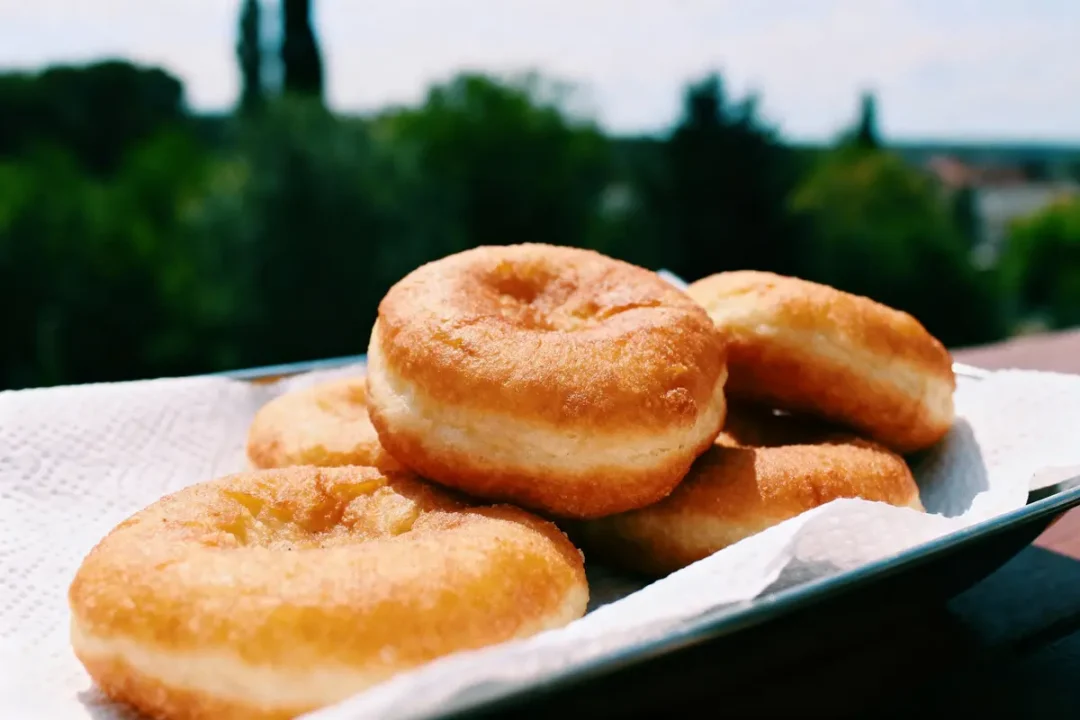 Beignets dorés empilés sur une assiette, serviette dessous, fond flou de verdure et ciel bleu.