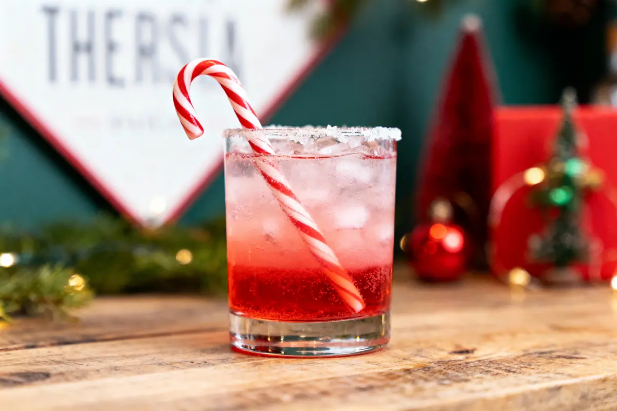 Verre de cocktail rouge avec sucre, canne en sucre d'orge, décorations de Noël en arrière-plan.