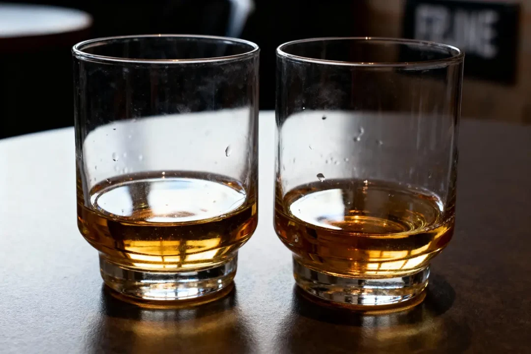 Deux verres à whisky à moitié remplis sur une table sombre.