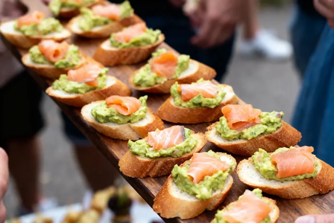 Tranches de pain avec guacamole et saumon fumé, servies sur une planche en bois, en extérieur.
