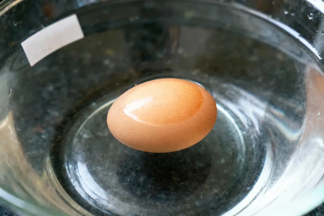 Un œuf brun flotte dans un bol en verre rempli d'eau.