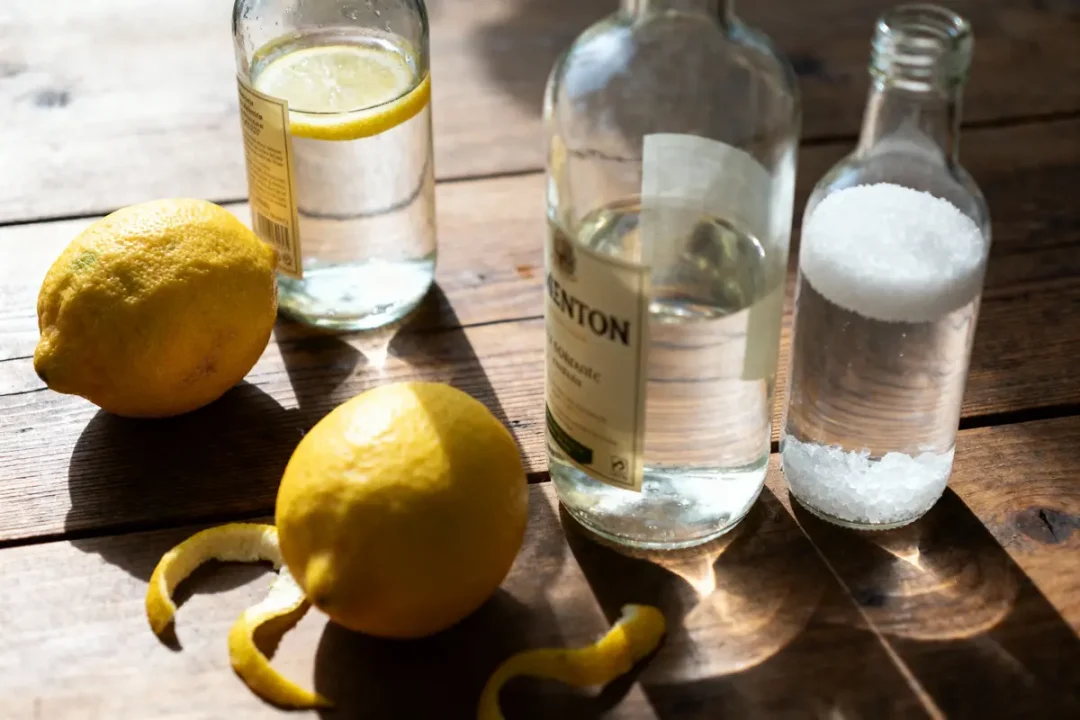 Deux citrons, bouteilles de verre avec eau et sel sur table en bois. Épluchures de citron.