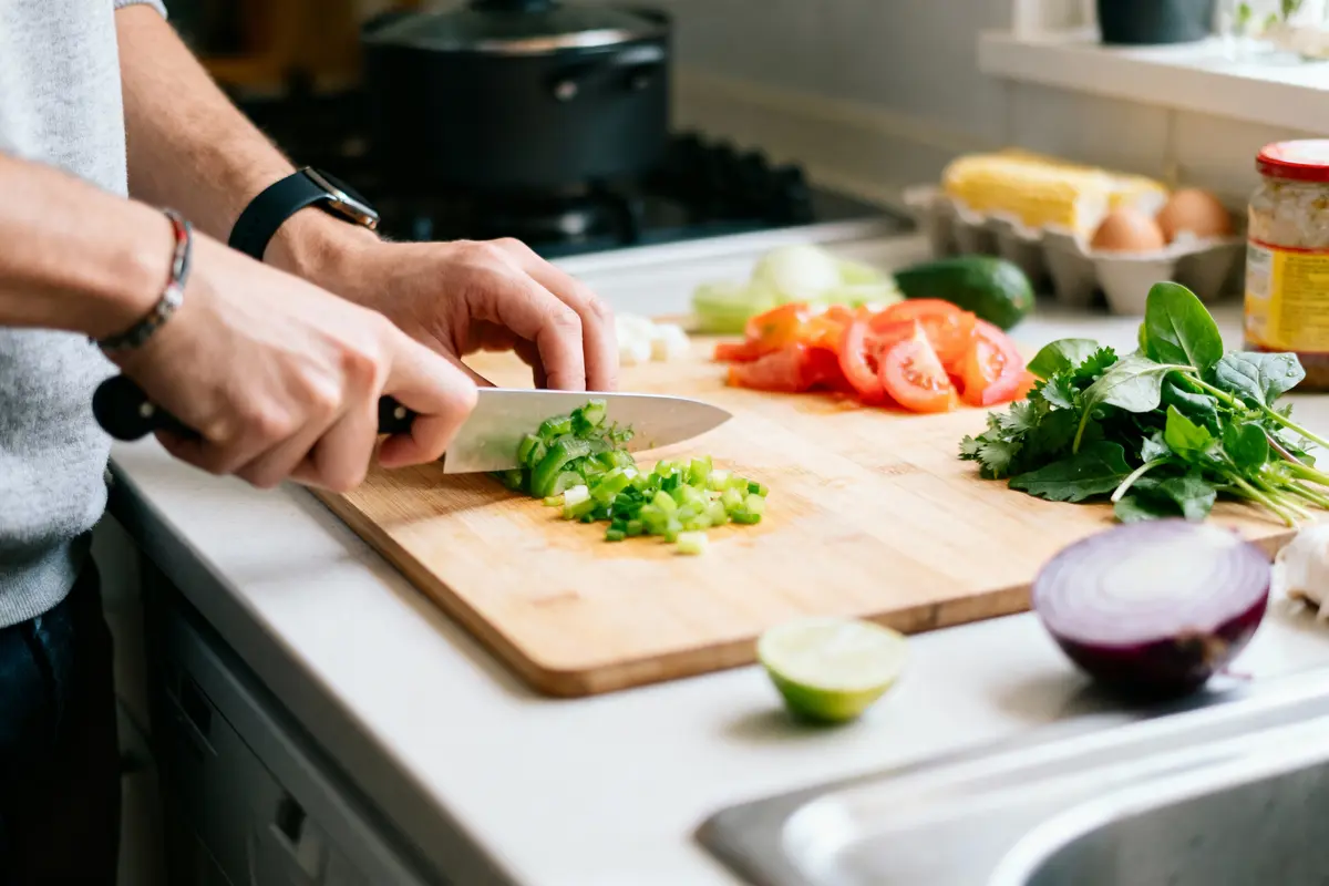 Personne coupant des légumes frais sur une planche en bois dans une cuisine lumineuse.