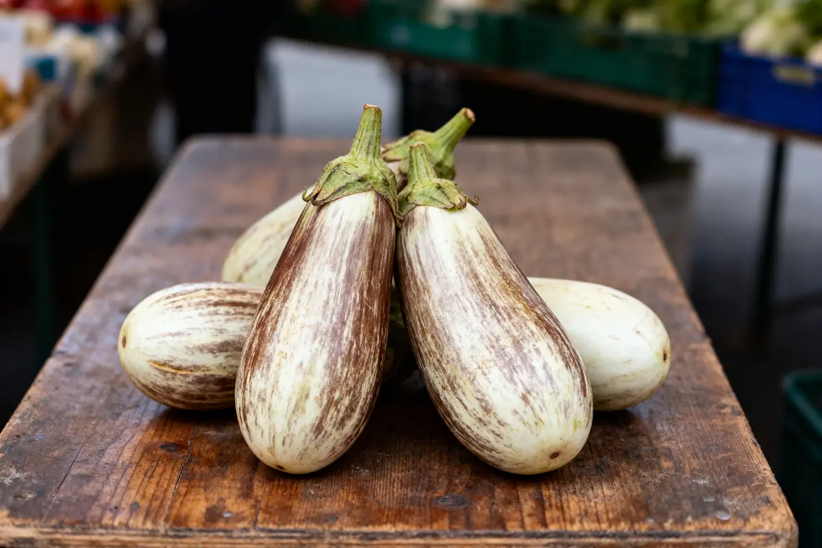 Aubergines blanches et brunes sur table en bois, marché en arrière-plan flou.