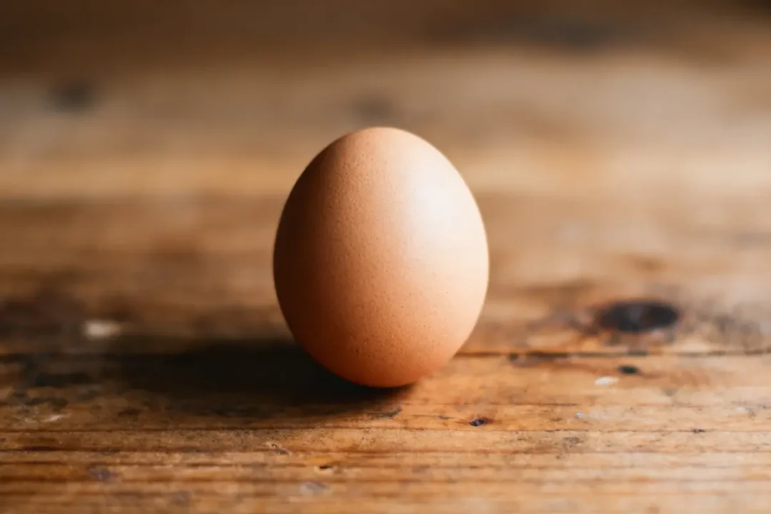Oeuf brun sur table en bois, éclairage doux, ton naturel.