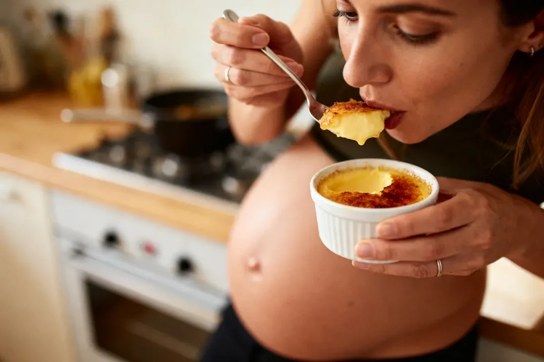 Femme enceinte dégustant un dessert crémeux avec une cuillère, dans une cuisine.