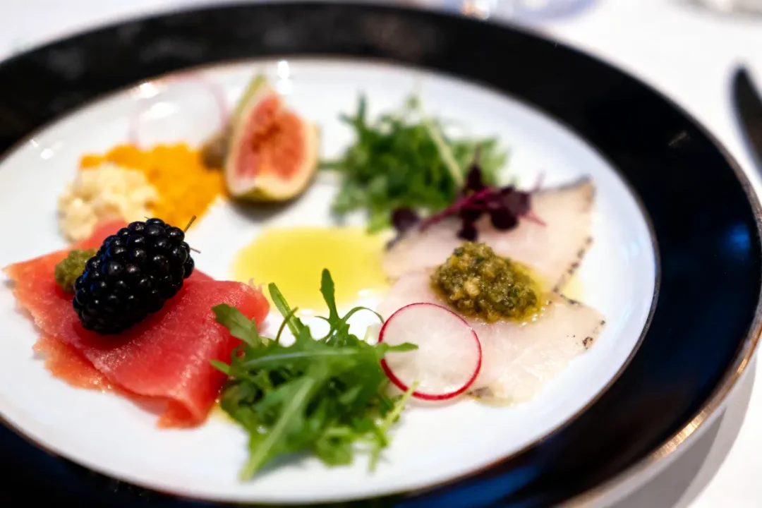 Assiette de cuisine gastronomique avec fruits, légumes, poisson, herbes, et sauce colorée, élégamment disposés.
