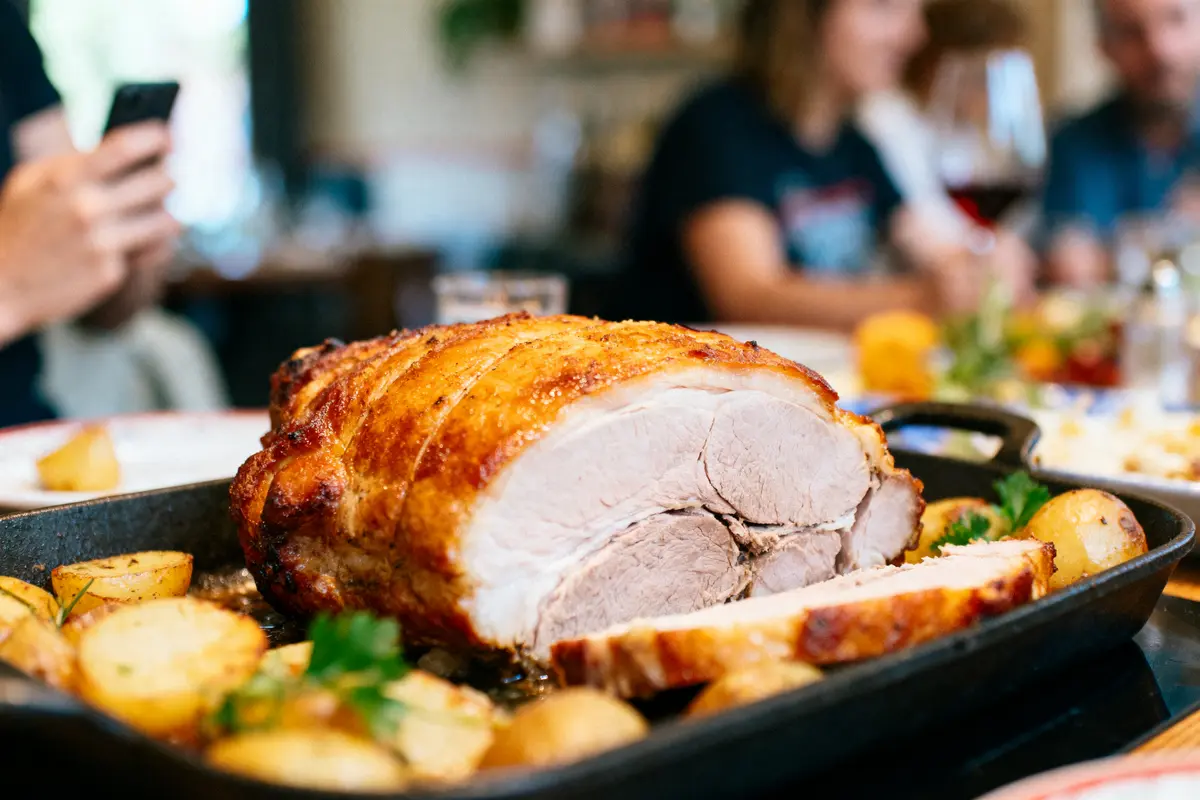 Rôti de viande dans un plat avec pommes de terre, personnes en arrière-plan flou.