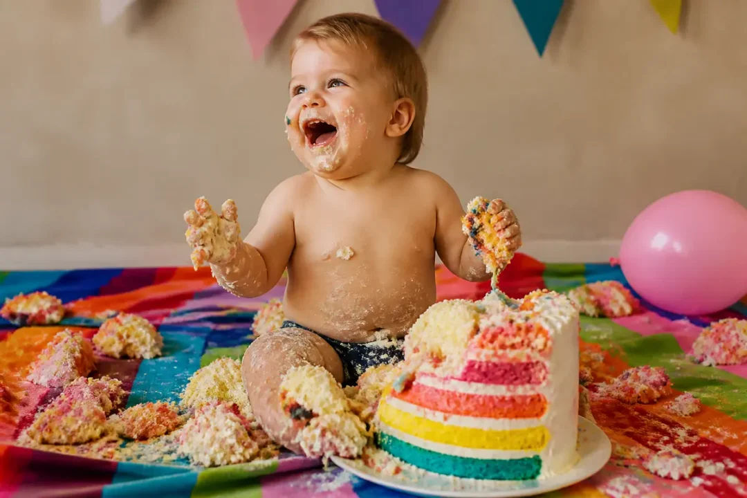 Bébé souriant jouant avec un gâteau arc-en-ciel lors d'une séance de cake smash